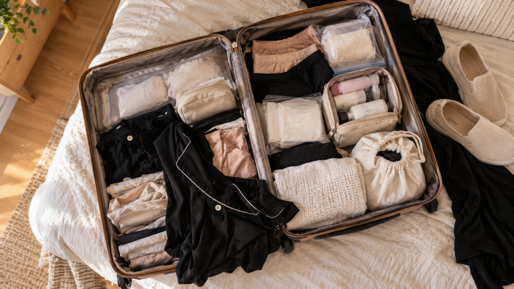 Mala de maternidade aberta vista de cima, organizada por grupos: roupas dobradas, calcinhas e absorventes em saquinhos, nécessaire de higiene, sacola para roupas usadas e sapatos ao lado